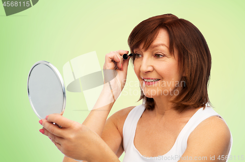 Image of smiling senior woman with mirror applying mascara