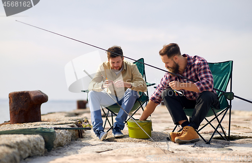 Image of friends adjusting fishing rods with bait on pier