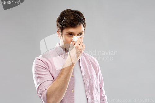 Image of unhealthy man with paper napkin blowing nose