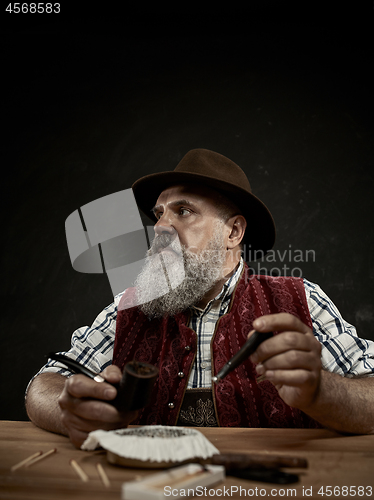 Image of bearded man clogs the tobacco in pipe