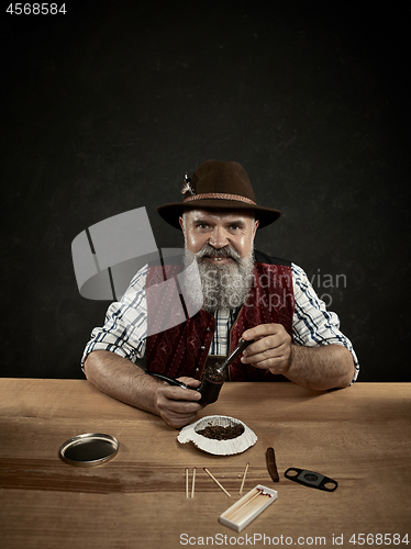 Image of bearded man clogs the tobacco in pipe