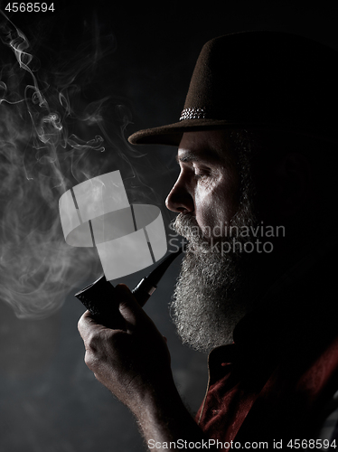 Image of Black and white dramatic portrait of senior smoking tobacco pipe