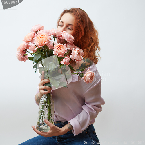 Image of Sexy girl with a bouquet of delicate pink roses in a transparent vase on a gray background with copy space. St. Valentine\'s Day