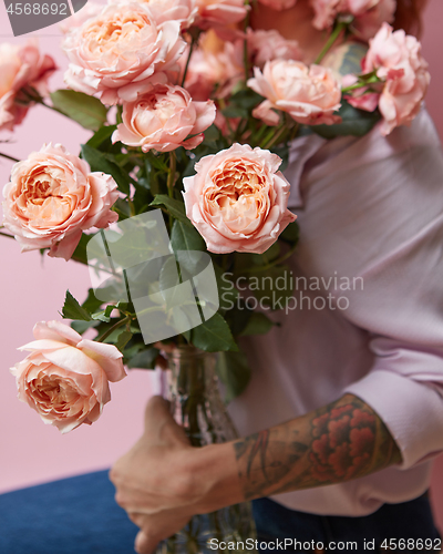 Image of A large bouquet of fresh pink roses in a glass vase holds a girl statue on a pink background. Valentine\'s Day Gift