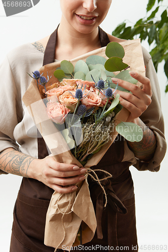 Image of Smilling girl florist with creative bouquet from fresh flowers roses in a paper on a light background. Close-up. Congratulation card.
