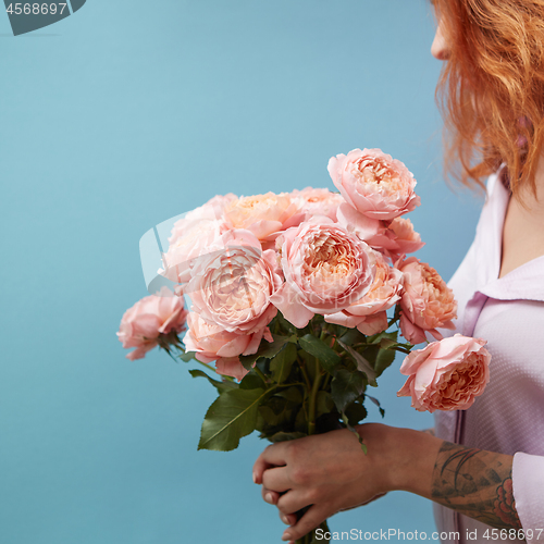 Image of Gentle pink roses in the hands of a girl with a tattoo on a blue background with copy space for text. Birthday present