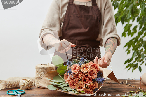 Image of Florist workplace - woman\'s hands are arranging a new bouquet with roses and decorative green leaves on a wooden table, process step by step. Place for text. Mother\'s Day.