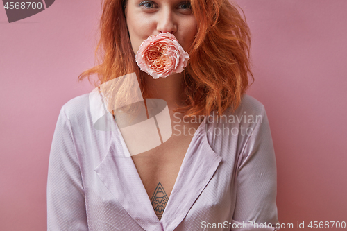 Image of Pretty woman holding a rose bud in her mouth around a pink backg