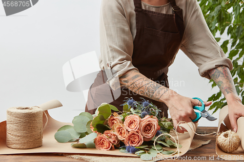 Image of Female florist is cutting paper for creating beautiful bouquet on a background of light wall. Place for text. Process of making bouquet step by step.