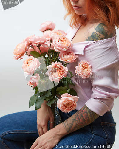 Image of A bouquet of pink roses in a vase holds a girl with a tattoo on a gray background with copy space. St. Valentine\'s Day