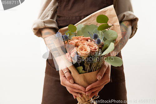 Image of Close-up of greeting bouquet from fresh roses, eryngium and green leaves a in a female\'s hands with tattoo on a gray background. Place for text. Gift for Mother\'s Day.