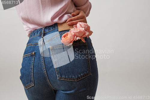 Image of Attractive woman\'s butt in a blue jeans and fresh roses living coral color in a back pocket on a light gray background, place for text. Congratulation card.