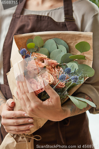Image of Florist in a brown apron with a bouquet of coral roses. Girl is holding a flowers in her hands. Close-up view. The gift to Mother\'s Day.