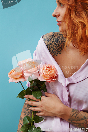 Image of Attractive female with tattoo on her shoulders and hands holds bouquet of coral roses on a blue background, place for text. A gift for Mother\'s Day.