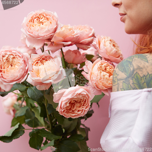 Image of A young girl with a tattoo is holding a bouquet of elegant pink roses around her pink background.