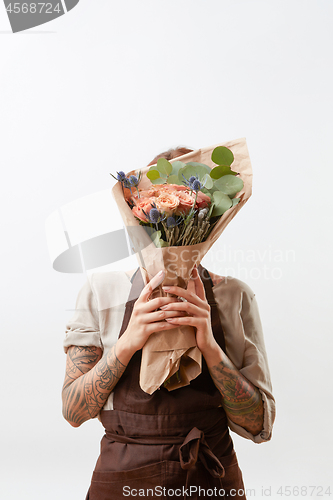 Image of Woman\'s hands with tattoo hold floral bouquet of living coral color roses and green leaf on a light background. Place for text. Concept of Mother\'s Day.