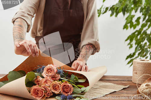 Image of Gardener girl make bouquet for a holiday from living coral roses and branches of green leaf on a wooden table on a light background. Mother\'s Day.