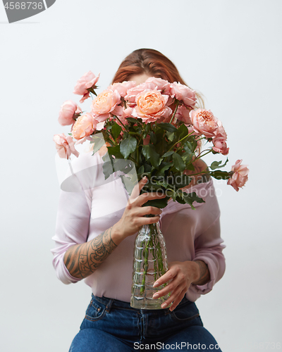 Image of A woman with a tattoo holding a large bouquet of pink roses in a glass vase around a gray background with copy space. Mother\'s Day Gift