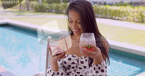 Image of Joyful ethnic young woman interacting with smartphone at poolside