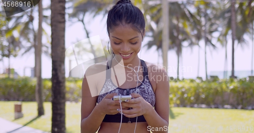 Image of Smiling Asian woman in earphones with smartphone in hand in park