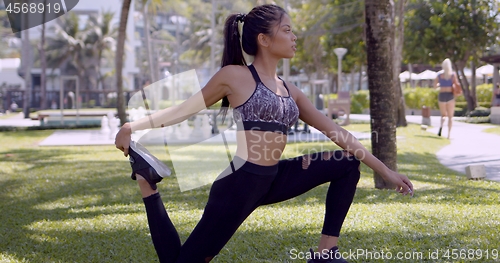 Image of Asian slim woman stretching leg in park