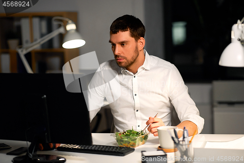 Image of businessman at computer eating at night office