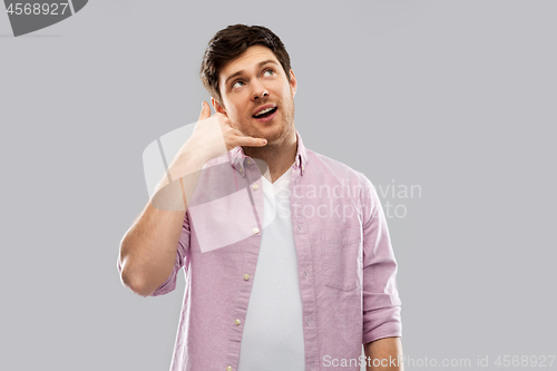 Image of young man showing phone call gesture over grey