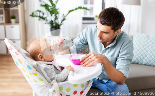 Image of father feeding happy baby in highchair at home