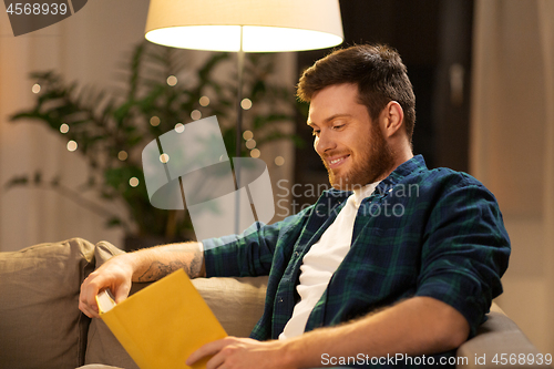 Image of happy young man reading book at home in evening