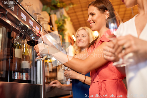 Image of happy women pouring wine from dispenser at bar