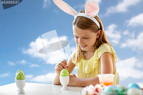 Image of happy girl coloring easter egg over blue sky