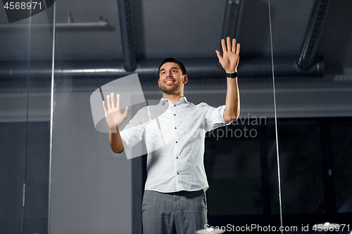 Image of businessman touching glass wall at night office