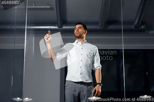 Image of businessman touching glass wall at night office