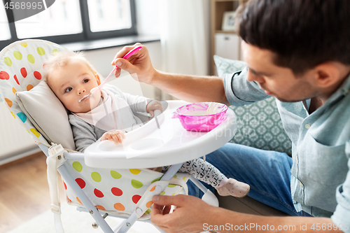 Image of father feeding happy baby in highchair at home