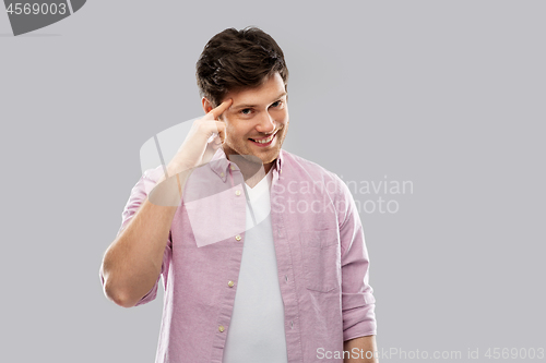 Image of smiling young man pointing finger to his head