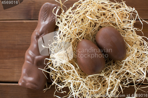 Image of chocolate bunny and eggs in straw nest on wood