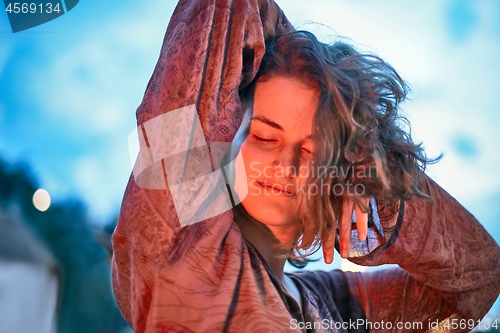 Image of Young woman dancing in the light of fire at dusk