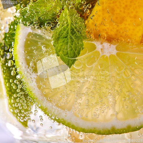 Image of Macro photo of fresh slices of green lime, yellow lemon and mint leaf with bubbles in a glass. Summer refreshing cocktail