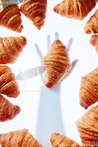 Image of French croissants frame with hand shadow taking bakery on a light background.