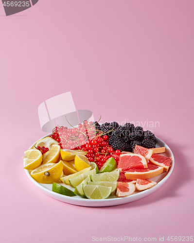 Image of Set of different citrus fruits and berries in a plate presented on a pink background with copy space. Healthy Vitamin Food