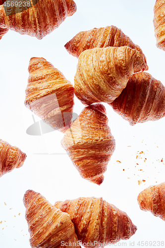 Image of Falling fresh french croissants with crumbs on a light background.