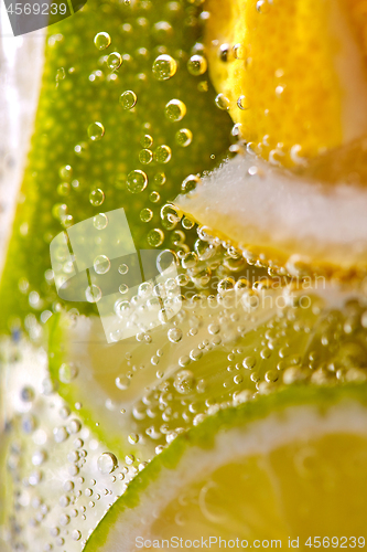 Image of Macro photo of freshly made lemonade with pieces of lime, lemon and bubbles in a glass. Summer refreshing drink