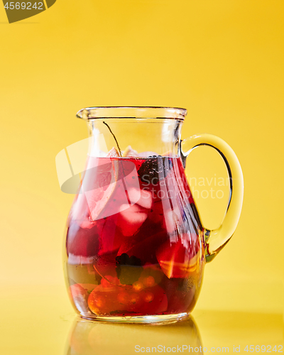 Image of Fruit berry homemade lemonade in a glass jug on a yellow background with copy space. Healthy drink
