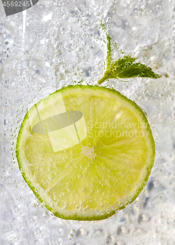 Image of Macro photo of a piece of lime and mint leaf in a glass with ice and bubbles. Cold summer drink concept