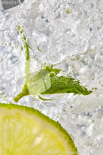 Image of Fresh mint leaf and a slice of lime with bubbles in a glass with ice. Macro photo of refreshing drink