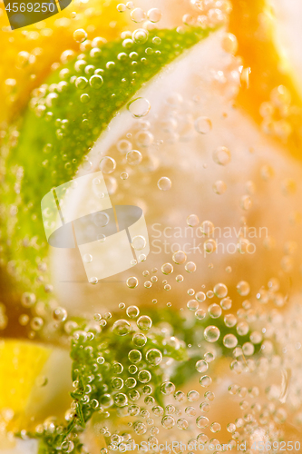 Image of Homemade refreshing drink made from lemon and lime slices with bubbles. Macro photo of summer healthy lemonade