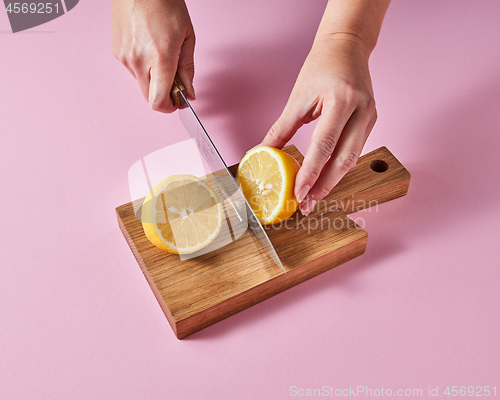 Image of Woman\'s hands cut a lemon on a wooden board with a knife around a pink background with copy space. Ingredient for summer drink