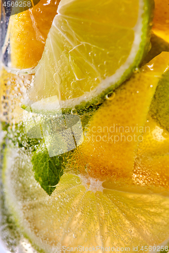 Image of Macro photo of sliced lemon and lime with a leaf of mint and bubbles in glass. Cool drink mojito