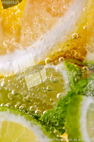 Image of Green leaf of mint, pieces of lemon and lime with bubbles in a transparent glass. Macro photo of summer cold mojito