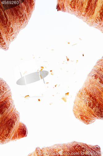 Image of Frame of fresh homemade croissants with crumbs on a light background.